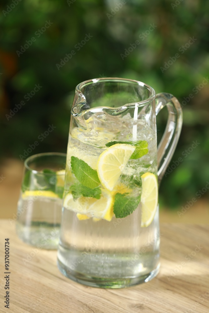 Refreshing lemonade with mint in jug and glass on wooden table against blurred green background, closeup Refreshing lemonade with mint in jug and glass on wooden table against blurred green background, closeup