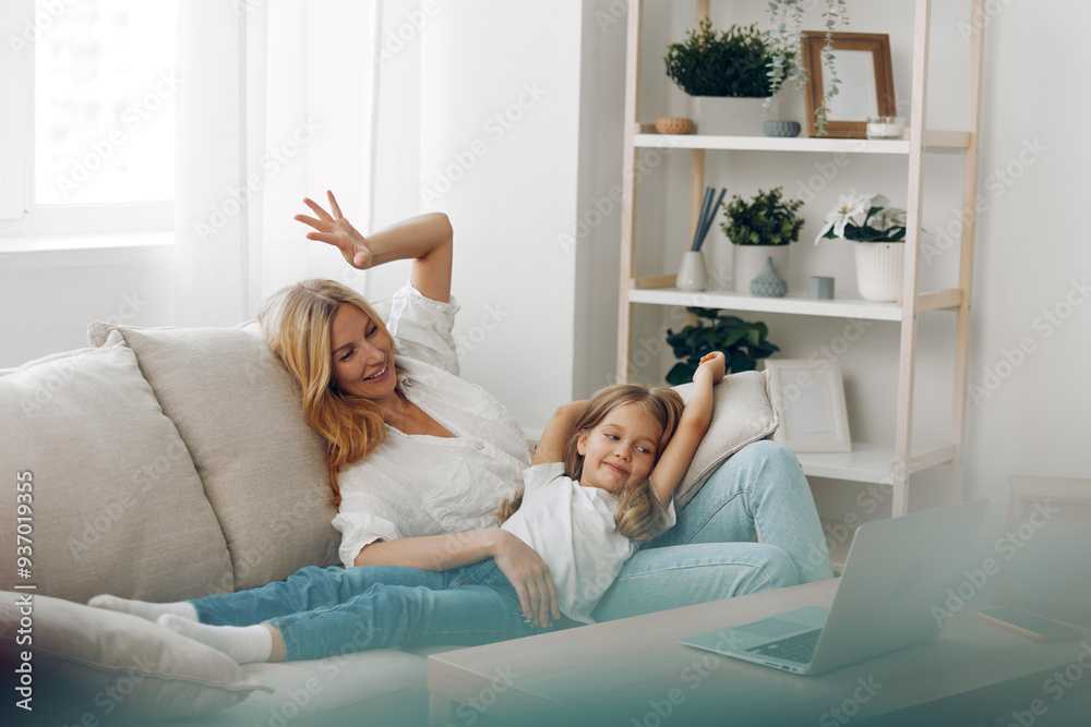 Joyful mother and daughter celebrating together on a cozy couch with hands raised in excitement and happiness Joyful mother and daughter celebrating together on a cozy couch with hands raised in excitement and happiness