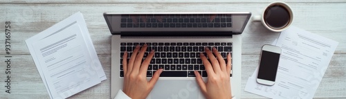 Aerial view of hands typing on a laptop with coffee and paperwork, showcasing a productive workspace environment.