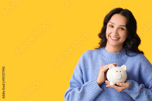 Pretty young woman with piggy bank on yellow background