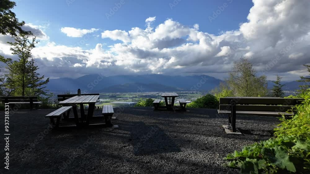 Empty picnic tables with a beautiful scenic mountain view. A gravel lookout with a vast valley, with mountains and clouds. Chilliwack, British Columbia, Canada. Empty picnic tables with a beautiful scenic mountain view. A gravel lookout with a vast valley, with mountains and clouds. Chilliwack, British Columbia, Canada.