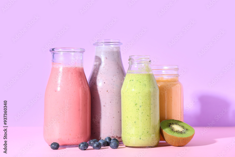 Bottles of different fresh smoothie with kiwi and blueberries on lilac background Bottles of different fresh smoothie with kiwi and blueberries on lilac background
