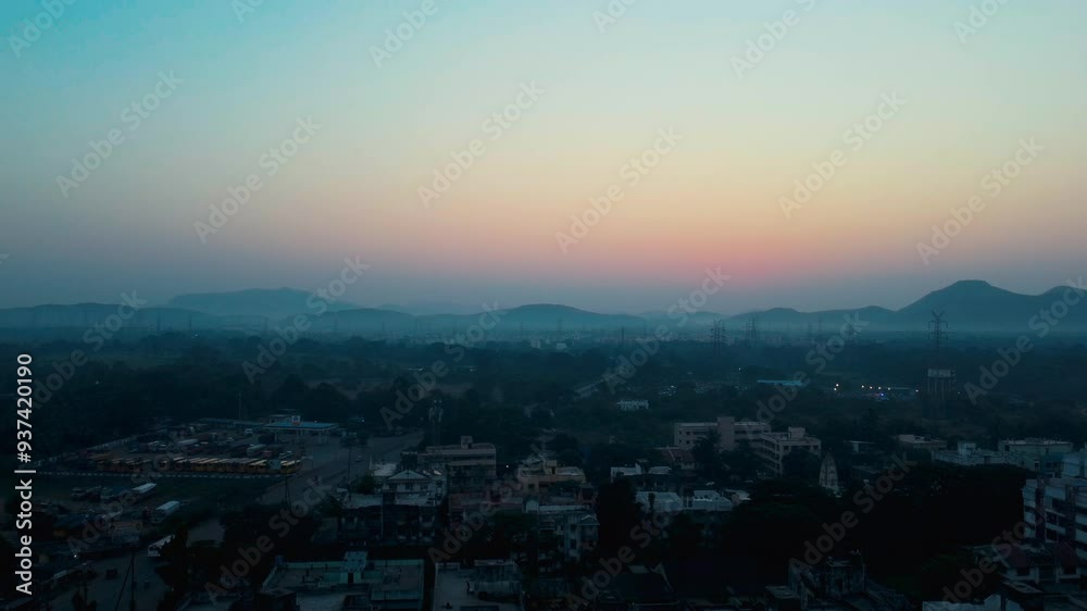 Drone ascends above peaceful town at dawn, sun slowly rises behind the mountains, sky is painted with soft morning colors with breathtaking view at Madhya Pradesh, India. Drone ascends above peaceful town at dawn, sun slowly rises behind the mountains, sky is painted with soft morning colors with breathtaking view at Madhya Pradesh, India.