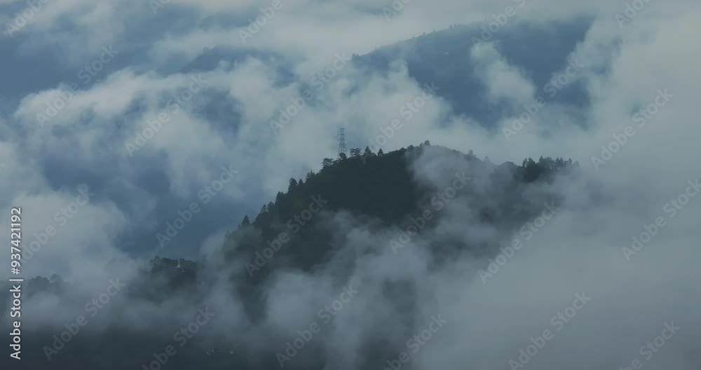 Drone shot of a powerline transmitter tower in misty, fog-covered hills of Nepal after monsoon rain. Showing rural technology and electricity infrastructure amidst a cloudy, atmospheric landscape. Drone shot of a powerline transmitter tower in misty, fog-covered hills of Nepal after monsoon rain. Showing rural technology and electricity infrastructure amidst a cloudy, atmospheric landscape.