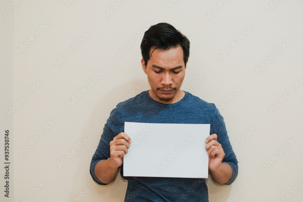 Serious Portrait of Southeast a Asian man activist holds piece of blank sheet of paper sign in his hands standing on cream background. Serious Portrait of Southeast a Asian man activist holds piece of blank sheet of paper sign in his hands standing on cream background.