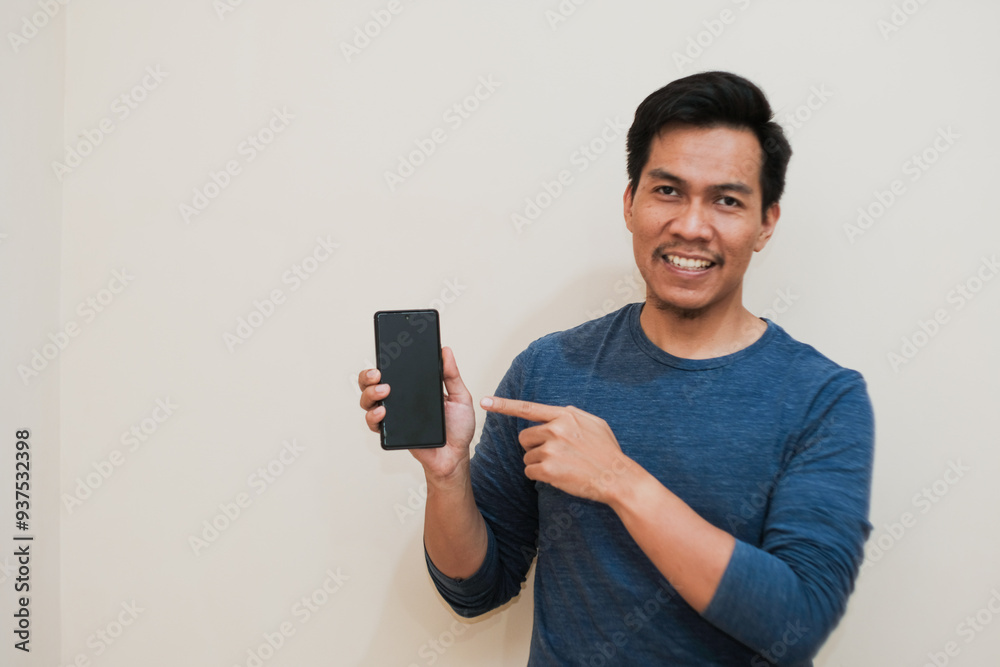 Portrait of Adult Southeast Asian man smiling happy while pointing finger to mobile phone screen, technology, positive emotion, copy space. Portrait of Adult Southeast Asian man smiling happy while pointing finger to mobile phone screen, technology, positive emotion, copy space.