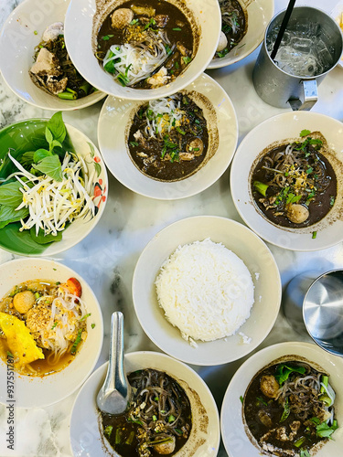 Thai boat noodles (Kuay Teow Reua) served in multiple bowls alongside a bowl of white jasmine rice and fresh vegetable garnishes, Asian cuisine, and cultural dining,  photo