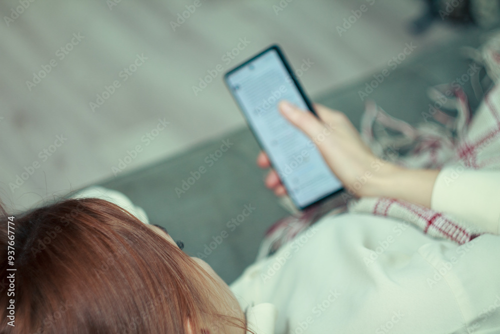 Fototapeta premium The girl is procrastinating: lying with a phone in her hands, a lazy expression on her face, a concentrated look