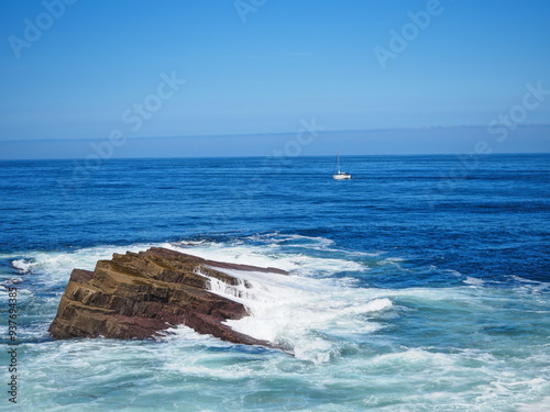 Rocas en el mar con un barco velero en el horizonte  photo