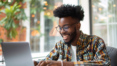 Young Smiling Man Typing on Laptop: A young man smiling while typing on a laptop