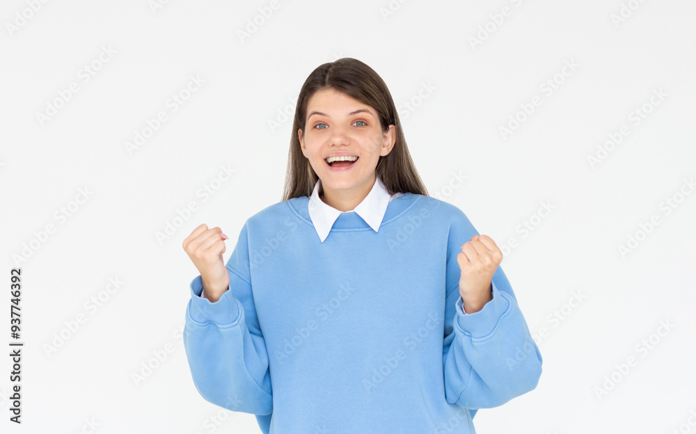 Portrait of ecstatic woman 20s wearing blue sweatshirt clenching fist like rejoicing victory or triumph isolated over white background Portrait of ecstatic woman 20s wearing blue sweatshirt clenching fist like rejoicing victory or triumph isolated over white background