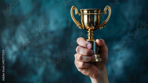 Hand holding golden trophy cup on dark blue background, copy space, success concept 