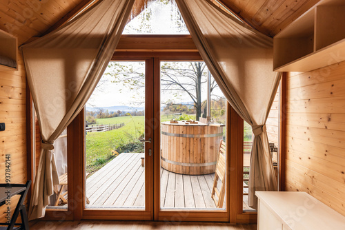 Empty glamping cabin with large panoramic windows and a private wooden hot tub on a terrace. Weekend getaway concept.