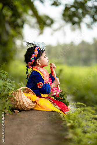 girl in a costume, adorable Indian baby in krishna kanha or kanhaiya dress posing with his flute  on white landscape background. sitting pose flower basket, happy, Vishu, Sreekrishna jayanthi,  photo