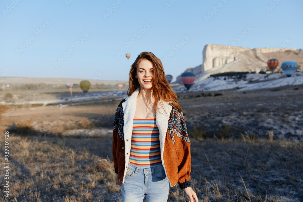 Woman standing in front of colorful hot air balloons in a vast field on a sunny day Woman standing in front of colorful hot air balloons in a vast field on a sunny day