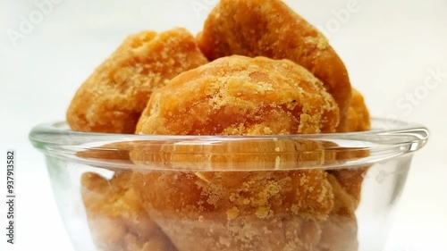 Organic Jaggery or Gur pieces in a glass bowl rotating against a clean white background, isolated micro shot. Brown cane sugar pieces in glass bowl isolated, front view photo