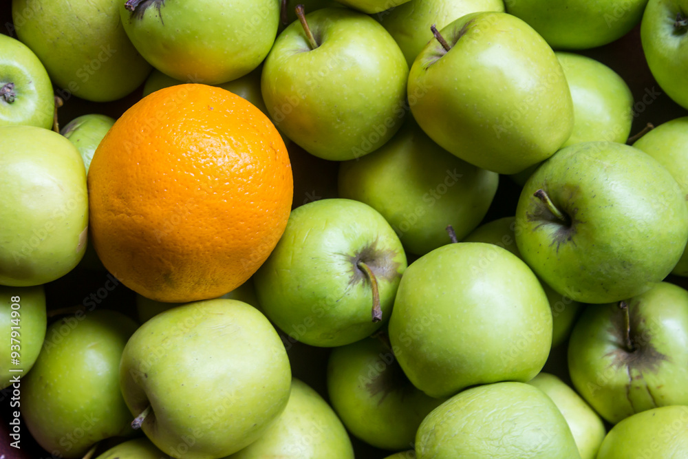 A mass of bright green apples, with a single orange A mass of bright green apples, with a single orange