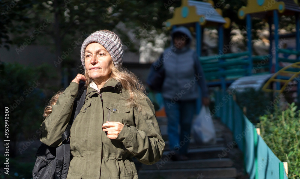 An old beautiful woman walks in the city thinking about motherhood near the playground.