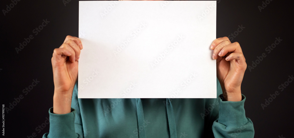 A girl holds a white sheet, paper with copyspace in her hands. A girl holds a white sheet, paper with copyspace in her hands.