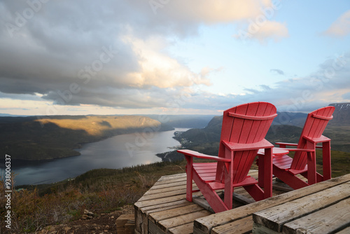 Two red adirondack chairs on a wooden deck overlooking Bonne Bay; Newfoundland and Labrador, Canada
