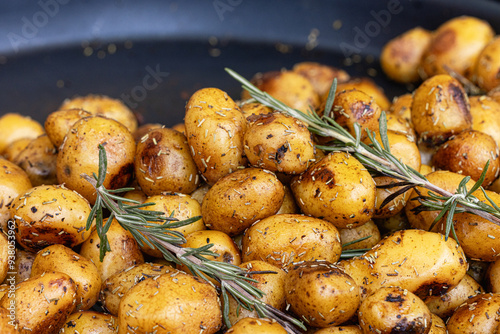 Close-up of roasted potatoes seasoned with a blend of aromatic herbs and spices, drizzled with olive oil, and garnished with rosemary and salt. Food concept photo