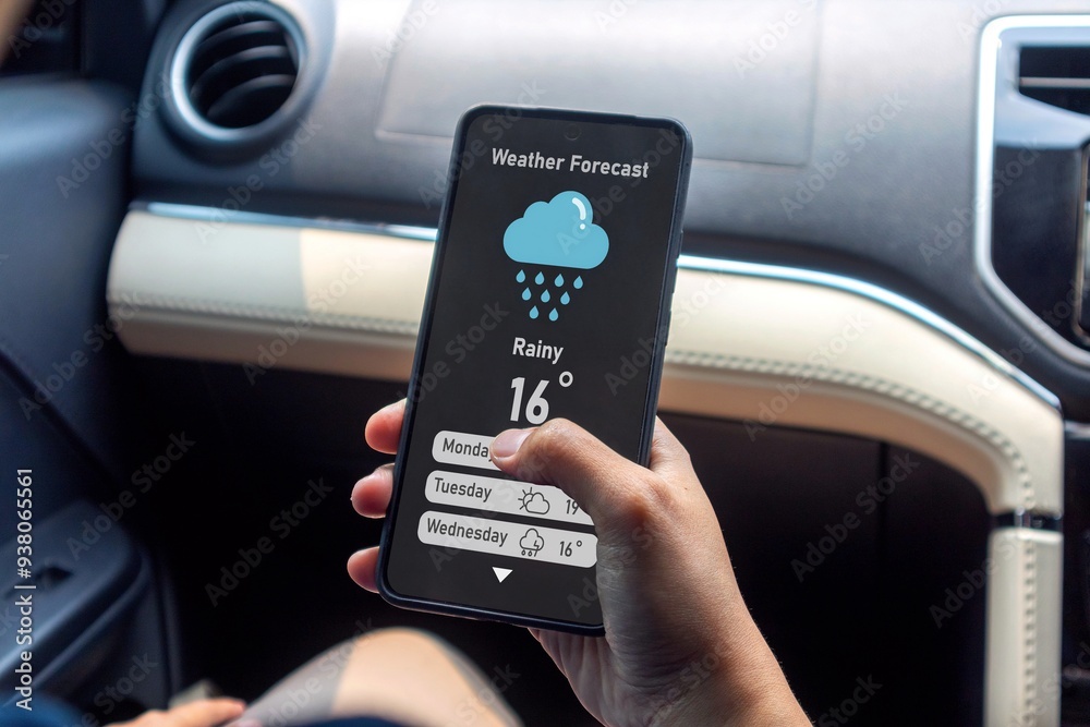 Hand of woman in a car holding a mobile phone to check weather forecast Hand of woman in a car holding a mobile phone to check weather forecast