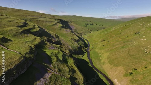 A lush landscape capturing the essence of Arncliffe with its meandering river through the green valley, framed by slopes and sunlight shadows photo