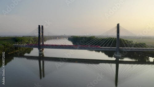 Aerial view of a Frecciarossa train crossing the high-speed rail bridge over the Po River near Piacenza, Italy. The tranquil evening setting reflects the modern marvel of Italian rail engineer