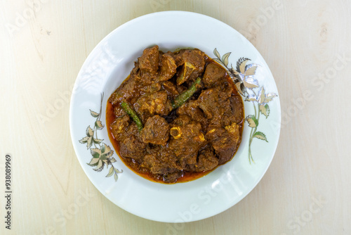 Delicious mutton curry in a white ceramic plate on a wooden background. Mutton bhuna is a popular, flavorful, and spicy Bangladeshi dish. Top view. photo
