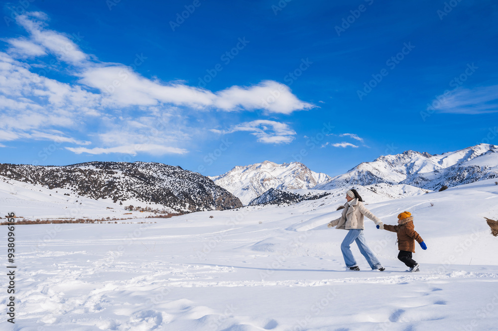 Mom and son running on a snow-covered slope against the backdrop of a mountain landscape in winter.