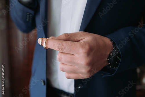 A man wearing a suit and holding a ring in his hand. The ring is a wedding band