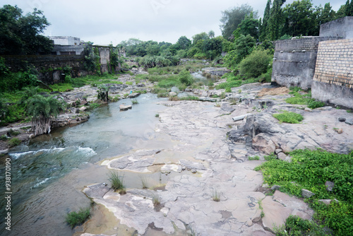 A serene watercourse winds its way through a lush environment, alongside the encroaching urban landscape