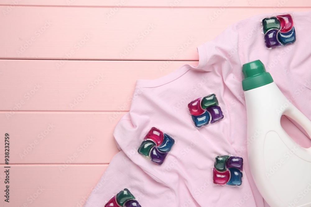 Laundry detergent in bottle, pods and t-shirt on pink wooden table, top view. Space for text Laundry detergent in bottle, pods and t-shirt on pink wooden table, top view. Space for text