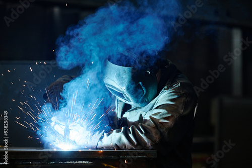 Metal worker performing welding with sparks flying in workshop, wearing protective gear and facemask for safety, focused on task in metalworking environment