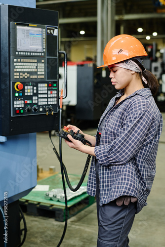 Worker in factory operating industrial machine using control panel wearing safety equipment including hard hat focusing on task in industrial setting