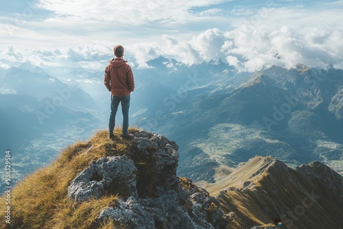 Man standing on mountain peak, admiring the breathtaking panoramic view of the vast valley and distant mountains under a cloudy sky.