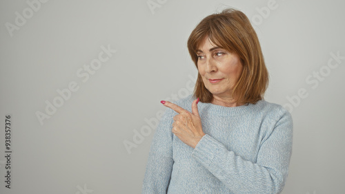 Slika na platnu Mature woman pointing sideways against a white background, embodying consideration and elegance