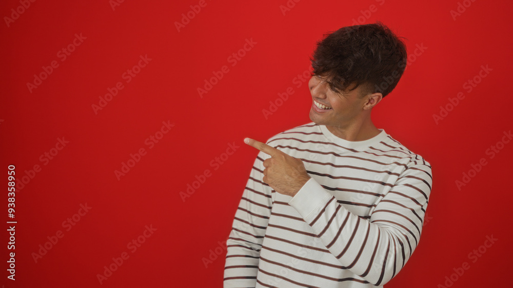 Young hispanic man in a striped shirt pointing and smiling against an isolated red background. Young hispanic man in a striped shirt pointing and smiling against an isolated red background.