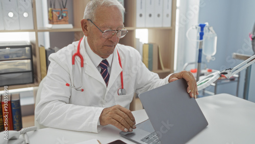 Senior caucasian man doctor in a clinic using a laptop in a hospital room.