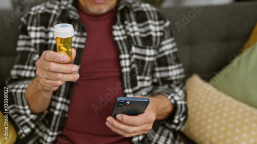 Mature man examining medication bottle while using smartphone at home, embodying health management and domestic life.