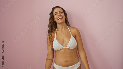 Attractive young hispanic woman smiling confidently in a white bikini over a pink background