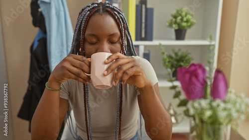 African american woman with braids sipping from a cup indoors, exuding a relaxed home atmosphere. photo