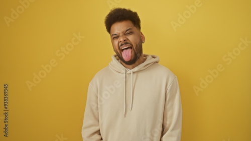 Handsome black man making a funny face against a yellow background while wearing a casual hoodie.