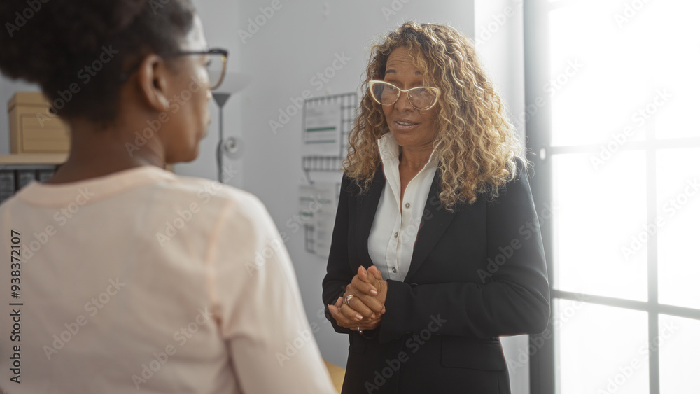 Obraz premium Women discussing business in an indoor office setting, highlighting professional work environment and collaborative efforts among employees
