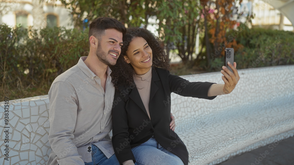 A smiling couple takes a selfie on a park bench, showcasing their love and happiness in a city environment. A smiling couple takes a selfie on a park bench, showcasing their love and happiness in a city environment.