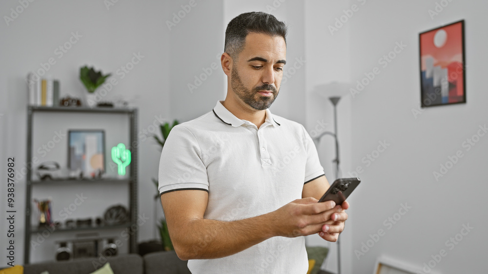 Hispanic man texting on smartphone in modern living room Hispanic man texting on smartphone in modern living room