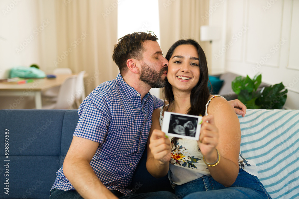 Man affectionately kisses his pregnant wife on the cheek as she holds a sonogram picture Man affectionately kisses his pregnant wife on the cheek as she holds a sonogram picture
