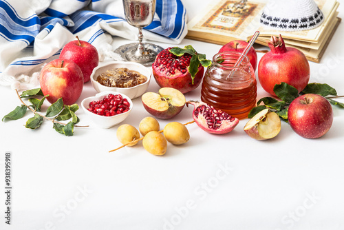 Jewish holiday Rosh Hashana festive table setting with plate, honey, apple ,pomegranates, dates, book of hebrew prayers, kiddush cup