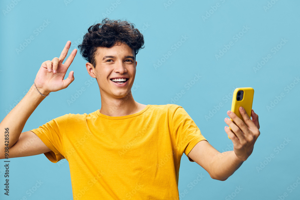 Happy young man taking a selfie with a yellow smartphone against a blue background, expressing joy and confidence Ideal for social media, youth culture, and technology themes