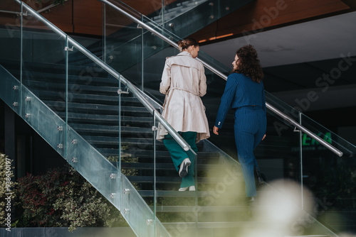 Fotografie Two businesspeople walking upstairs in a modern office building, engaging in a work discussion